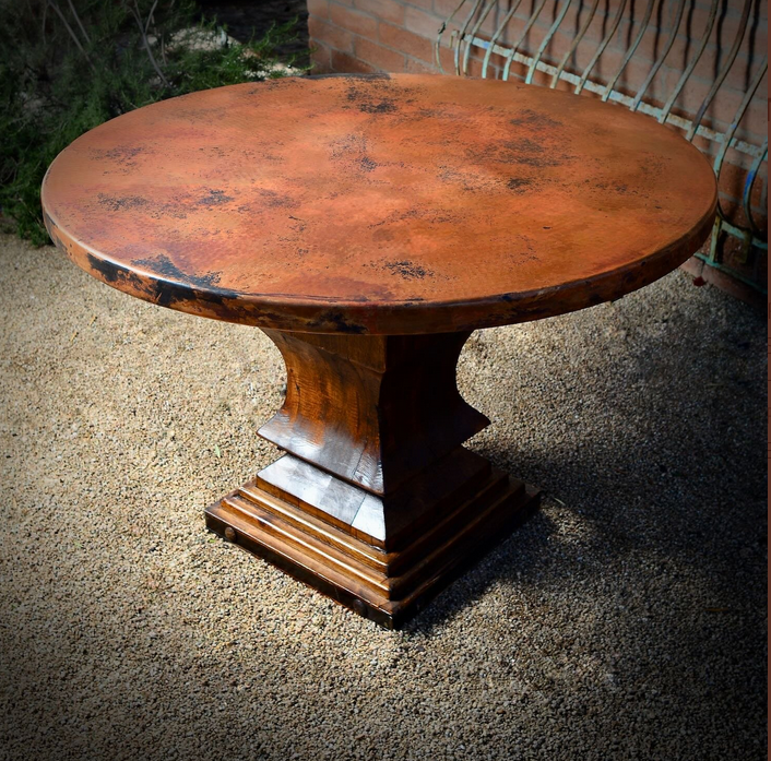 Round dining table with a hammered copper top on a stepped wooden pedestal base