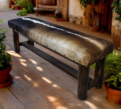 Long dark wood bench with a cowhide seat and nailhead trim on a wooden porch