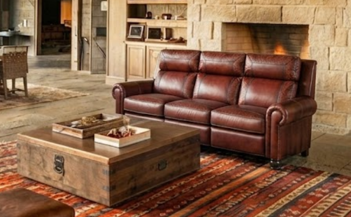 Rolled-arm brown leather reclining sofa beside a stone fireplace with a rustic trunk coffee table
